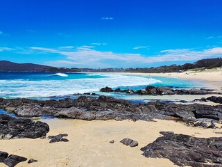 Scenic Coastal Beach with Rocky Shoreline and Ocean Waves under Clear Blue Sky