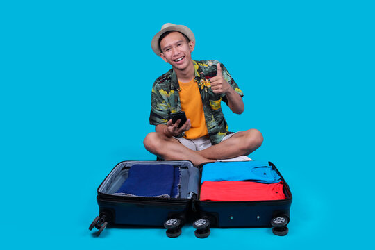 Traveler Guy Using Phone and Showing Thumb Up While Sitting Near Baggage Isolated on Blue Background