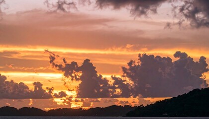 A dramatic sunset paints the sky with vibrant hues of orange and gold, as dark clouds gather above a silhouetted coastline.