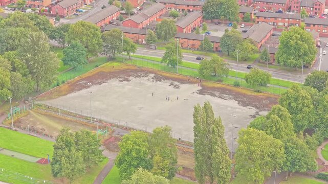 Cleared plot in Salford, likely a former outdoor court now under groundwork amidst housing and green patches&mdash;suggesting upcoming redevelopment or sports facility enhancement, static aerial shot.
