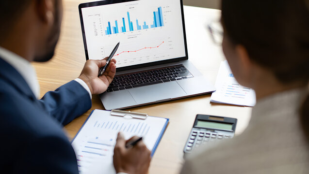 Strategic Business Analysis: Focused individuals review financial data on a laptop and document, strategizing business decisions. - Powered by Adobe