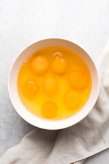 Organic raw eggs in a white mixing bowl for baking, top view of whole raw eggs on white background