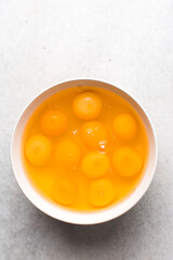 Organic raw eggs in a white mixing bowl for baking, top view of whole raw eggs on white background