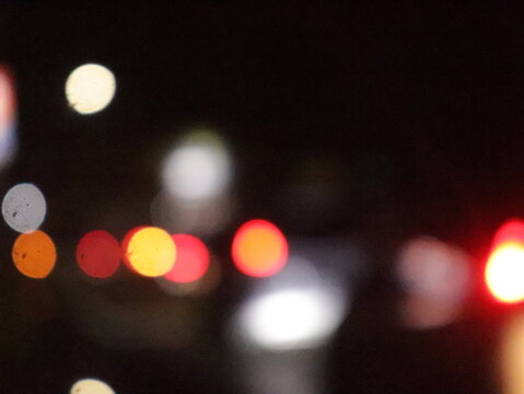 A stunning bokeh effect at night, showcasing blurred city lights in vibrant tones of red, orange, yellow, and white glowing softly against a dark black background.
