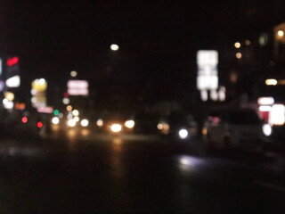 Out-of-focus city street at night, filled with blurred car headlights, glowing taillights, and scattered streetlights that create a dreamy bokeh effect. The image reflects the hustle of nightlife