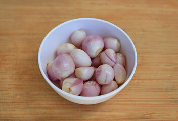 Peeled onion cloves in white bowl on bamboo wooden background, preparation process of onion for cooking.