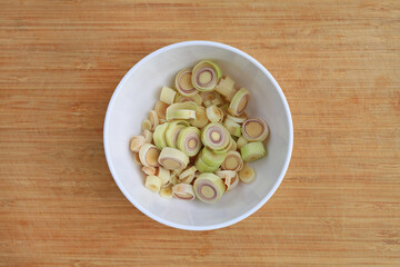 Chopped lemon grass in white bowl against wooden background, preparation process of lemon grass for cooking. Top view.