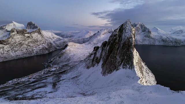 Cinematic aerial view of Segla peak on Senja Island, Norway, steep snow-covered cliffs above icy fjord, dramatic arctic landscape with rugged mountains and winter wilderness