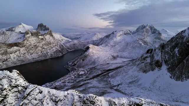 Cinematic aerial view of Segla peak on Senja Island, Norway, steep snow-covered cliffs above icy fjord, dramatic arctic landscape with rugged mountains and winter wilderness