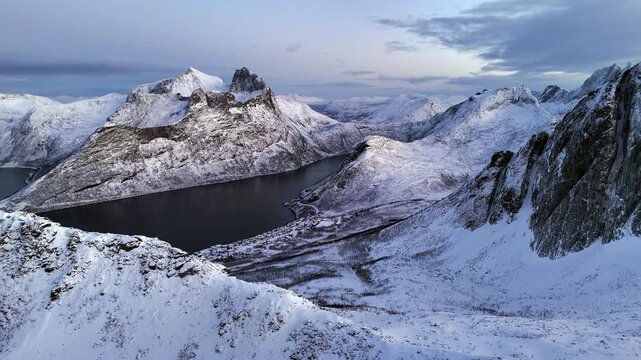 Cinematic aerial view of Segla peak on Senja Island, Norway, steep snow-covered cliffs above icy fjord, dramatic arctic landscape with rugged mountains and winter wilderness