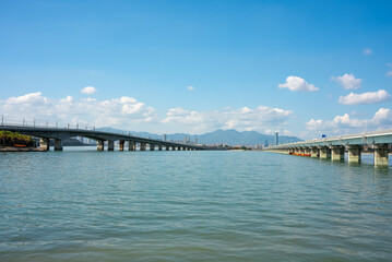 Obraz premium Two long bridges span the calm waters leading to the urban cityscape and distant mountains under the clear blue sky of Xiamen.