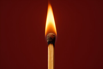 A single wooden matchstick ignited with a small glowing orange flame, captured against a solid red background.