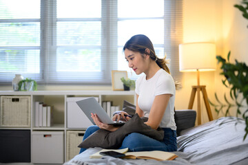 Asian female in casual clothing focused on remote work with laptop on sofa