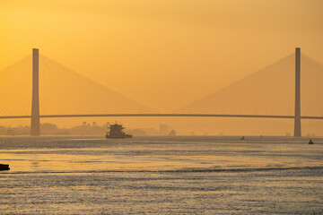Obraz premium A ship sails on Yangtze River under a large cable stay bridge in Ezhou, Hubei, China, during a golden sunset.