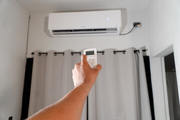Person holding remote control, pointing at air conditioner unit in home interior