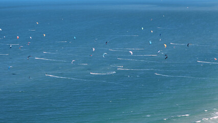 Many Colorful kites flying over blue sea with kiteboarders surfing waves