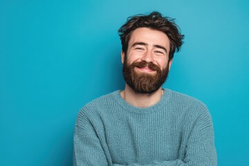 Obraz premium Bearded young man alone against a blue backdrop smiling cheerfully