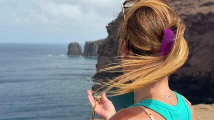 Female traveler navigating coastal terrain of Gran Canaria, holding compass with iconic Roque Partido landmark rising dramatically in rocky background during summer adventure journey - Powered by Adobe