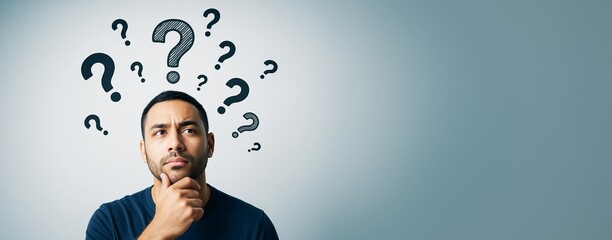 Thoughtful man surrounded by question marks on gradient background with copy space, representing decision making and problem solving concept.