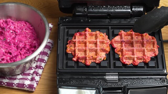Making vegetarian beetroot and zucchini waffles with herbs in waffle maker, close up. Vegetable waffles for eat made with waffle iron with teflon coating
