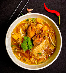 Braised chicken noodle soup in a bowl with fresh herbs and green onions. Tender chicken and flavorful broth with soft noodles, traditional Thai comfort food.