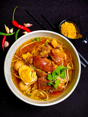 Thai braised pork leg noodle soup served in a bowl with fresh herbs, boiled egg, and green onions. Tender pork leg and rich savory broth with soft noodles, a traditional and appetizing Thai comfort fo