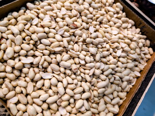 Shelled peanuts displayed in a wooden crate at a local market, showcasing their natural color and texture under bright lighting in the afternoon