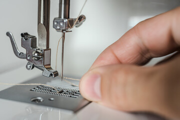 Hand of tailor with sewing machine thread to start sewing. Hand guiding thread through sewing machine needle, detailed macro view of threading process