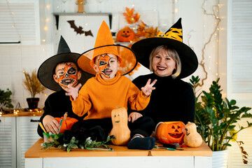 Halloween, a happy family a mother with children in festive costumes and makeup is preparing for Halloween at home in the kitchen by coloring and carving pumpkins and scaring everyone