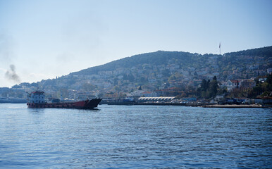 Fototapeta premium Cargo Ship Docked Near a Bustling Coastal Town With Hills in the Background