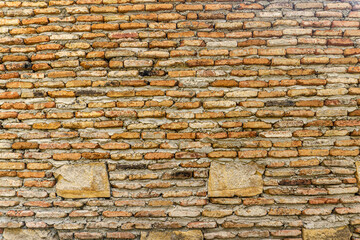 Old wall brickwork bonded with light mortar with occasional inserts of large stones. Some places of mortar are weathered, some are plastered over the bricks. Texture and grain are clearly visible