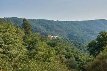 Naklejka premium Small village on a mountainside covered in vegetation, seen from the Pesqueiras Viewpoint in Galicia, Spain