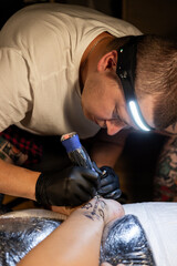 Tattoo artist carefully working on a client’s leg design under focused light. Concept of precision, artistry, creativity, and modern body art in a professional tattoo studio