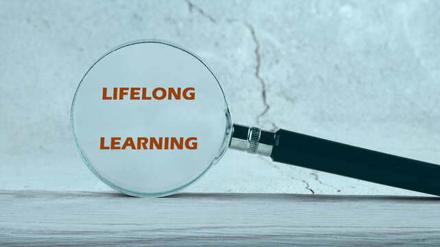 A magnifying glass highlights the phrase lifelong learning against a textured background, emphasizing continuous education in business
