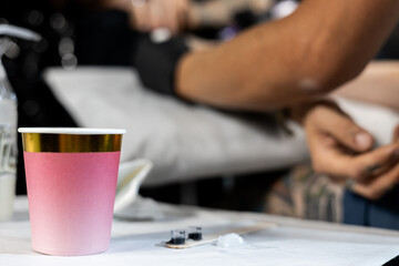 Close-up of disposable tattoo ink cups and a pink cup on the artist's table, with tattooist's gloved hands in the background. Tattoo studio setup before inking session.