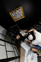 Tattooed man talking on the phone while getting a tattoo in a professional studio. A candid moment...