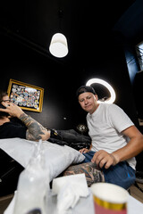 Tattoo artist focused on his work in a modern studio, preparing equipment and inking a client's arm. Captures the precision and concentration behind the art of tattooing