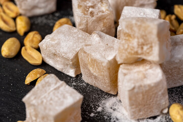 Turkish delight in sugar with nuts inside, scattered oriental sweets Turkish delight with peanuts on a slate board, close up