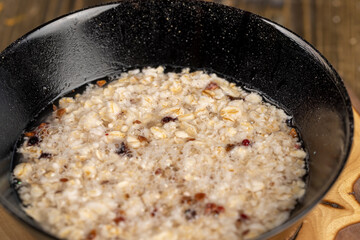 boiled oatmeal porridge with dried berries and fruits in a black bowl , cooking instant oatmeal porridge