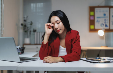 Tired asian businesswoman rubbing eyes at office desk