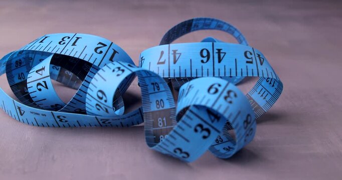 Blue measuring tape used in tailoring falls onto a concrete table, illustrating tools, fabric design, and measurement in fashion.