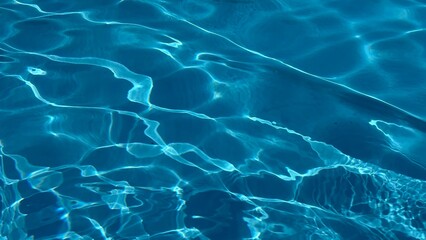 Horizontal photo of deep blue rippling water in swimming pool with sun reflection and magic feel.