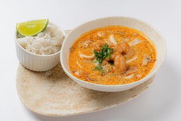 A flavorful bowl of shrimp soup, vibrant with spices and served alongside fluffy rice and lime