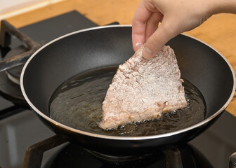 The cook places a breaded pork chop into the heated frying fat in a pan,