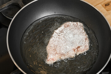 Traditional fried pork chop coated in breadcrumbs and fried in hot fat in a metal pan,