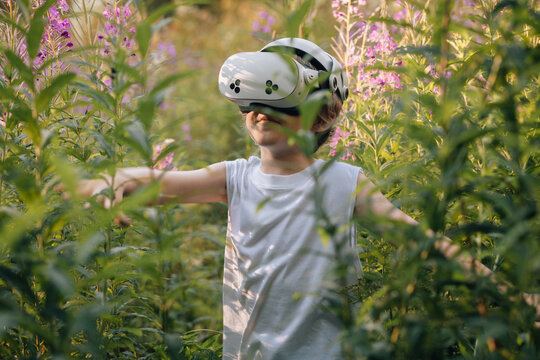 Man child in virtual reality glasses playing in flowers in forest