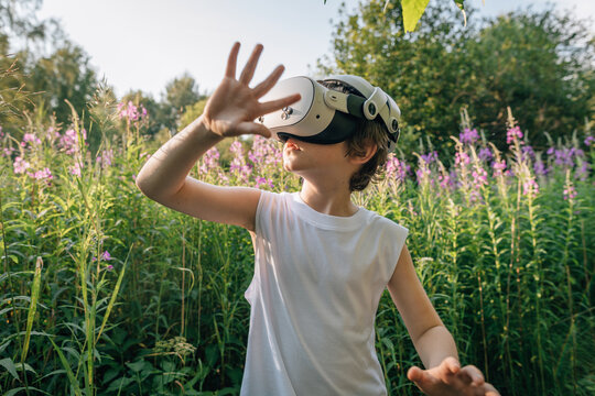 Man child boy in virtual reality glasses in flowers and grass plays