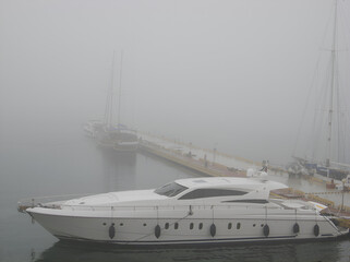 Fototapeta premium Elegant yacht docked at pier on a foggy morning, sailing boats hidden in mist, tranquil seascape symbolizing mystery, luxury travel, marine leisure and nautical atmosphere