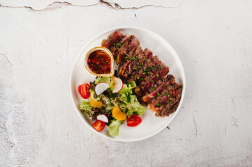 Grilled Steak with Side Salad and Orange Sauce on White Plate