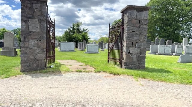Time lapse of Jewish Cemetery with large headstones passing through a metal stand alone gate during the day as clouds pass through